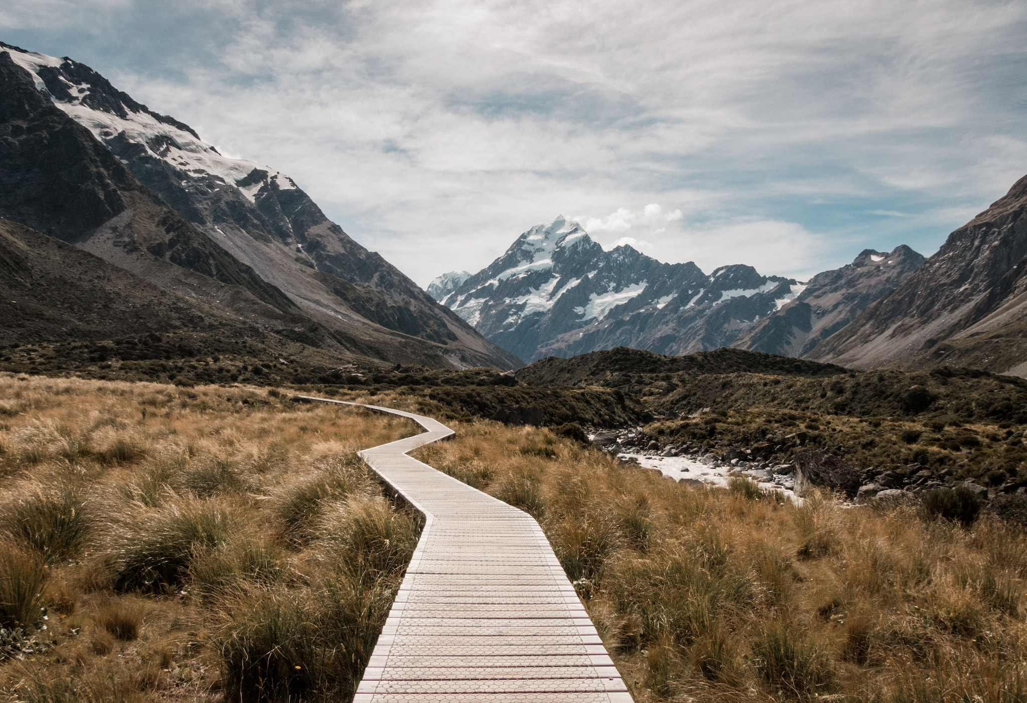 Wooden boardwalk winding through a mountain valley toward snow-capped peaks — representing hope and a path forward